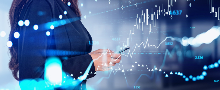 A businesswoman in a suit points at a screen displaying graphs while holding a pen, indicating data analysis.