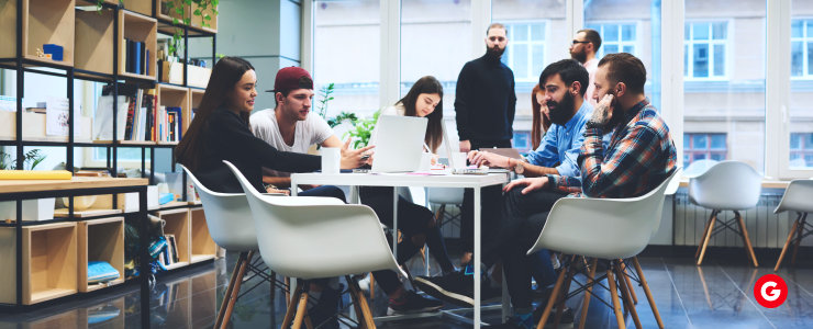 A group of diverse individuals engaged in discussion around a conference table in a modern office setting.
