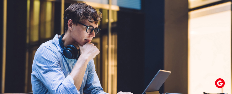 A man wearing glasses sits at a table with a laptop, analyzing currency volatility during elections.